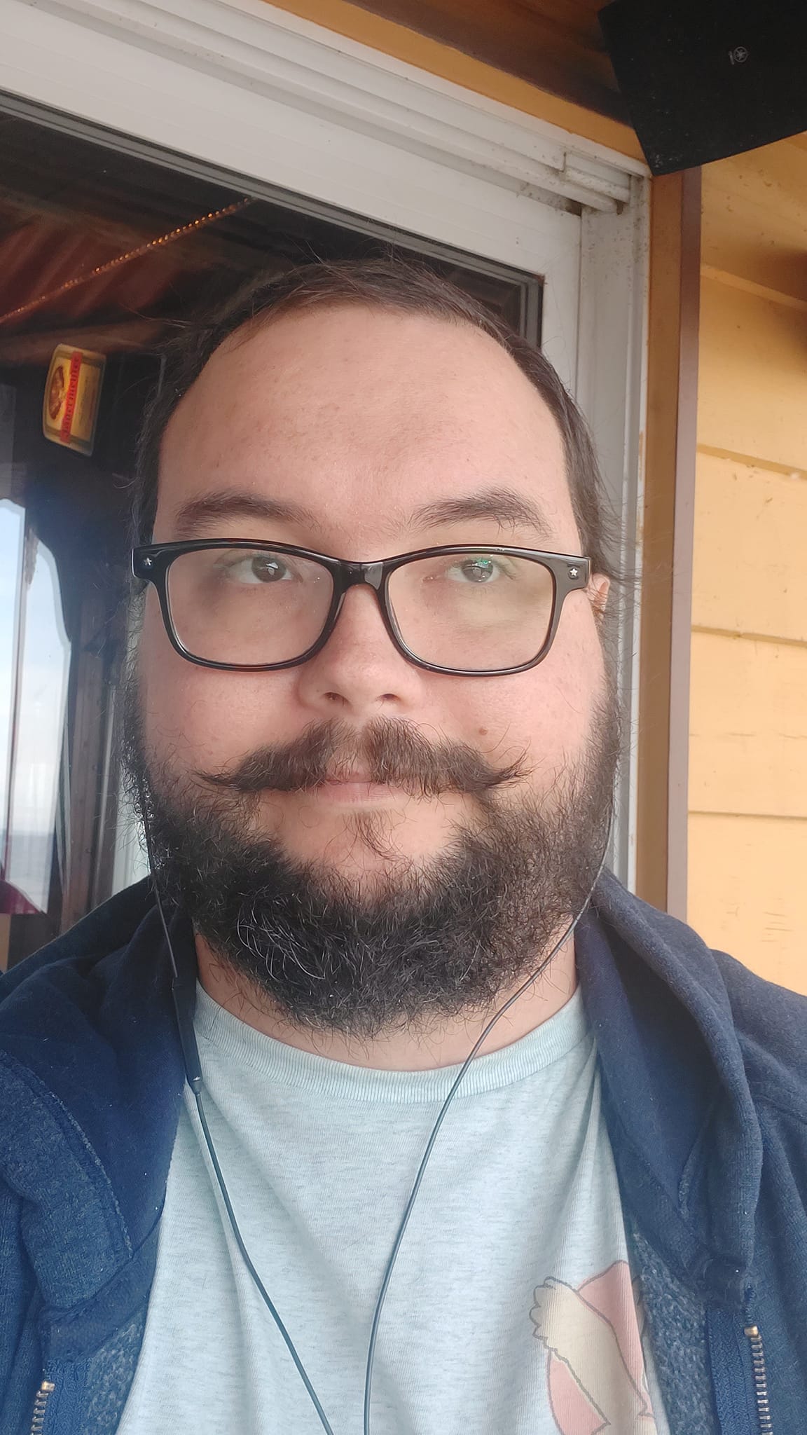 A man short hair and bushy facial hair sits on a restaurant patio